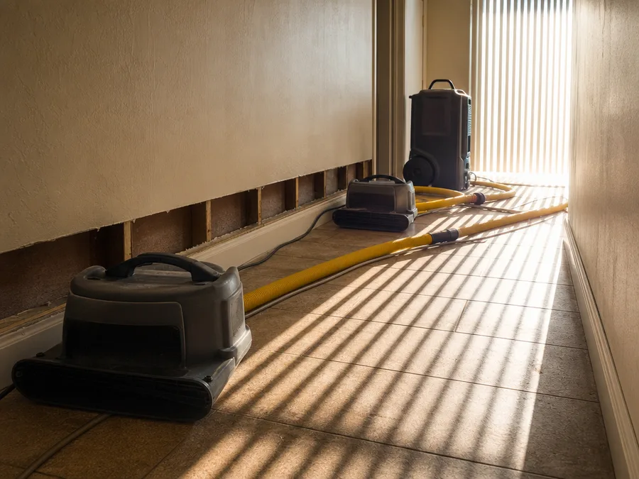 Drying equipment standing on a tiled floor beside a cut line of removed baseboard